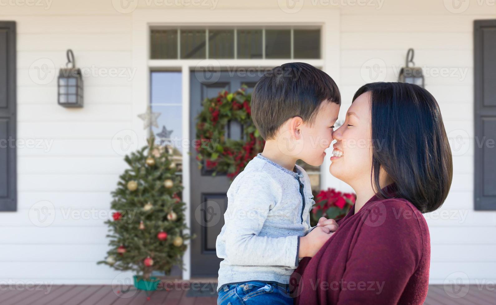 Chinese Mother and Mixed Race Child Rubbing Noses Standing on Christmas Decorated Front Porch photo