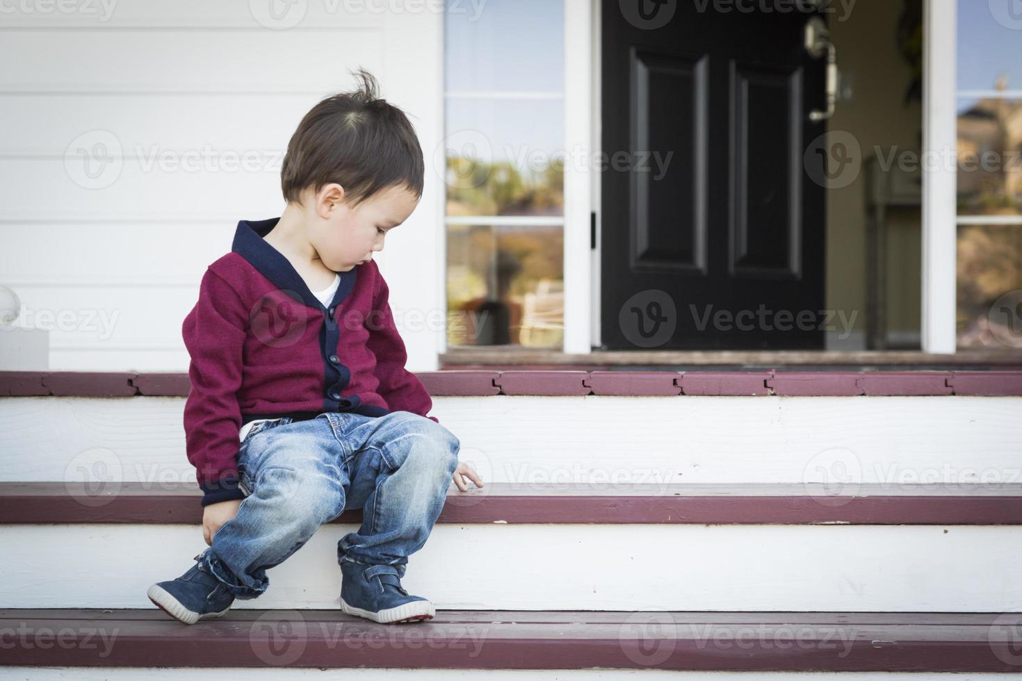 Melancholy Mixed Race Boy Sitting on Front Porch Steps photo
