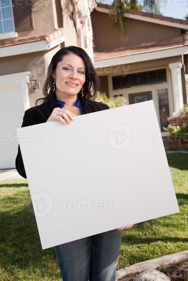 atractiva mujer hispana sosteniendo un cartel en blanco frente a la casa foto