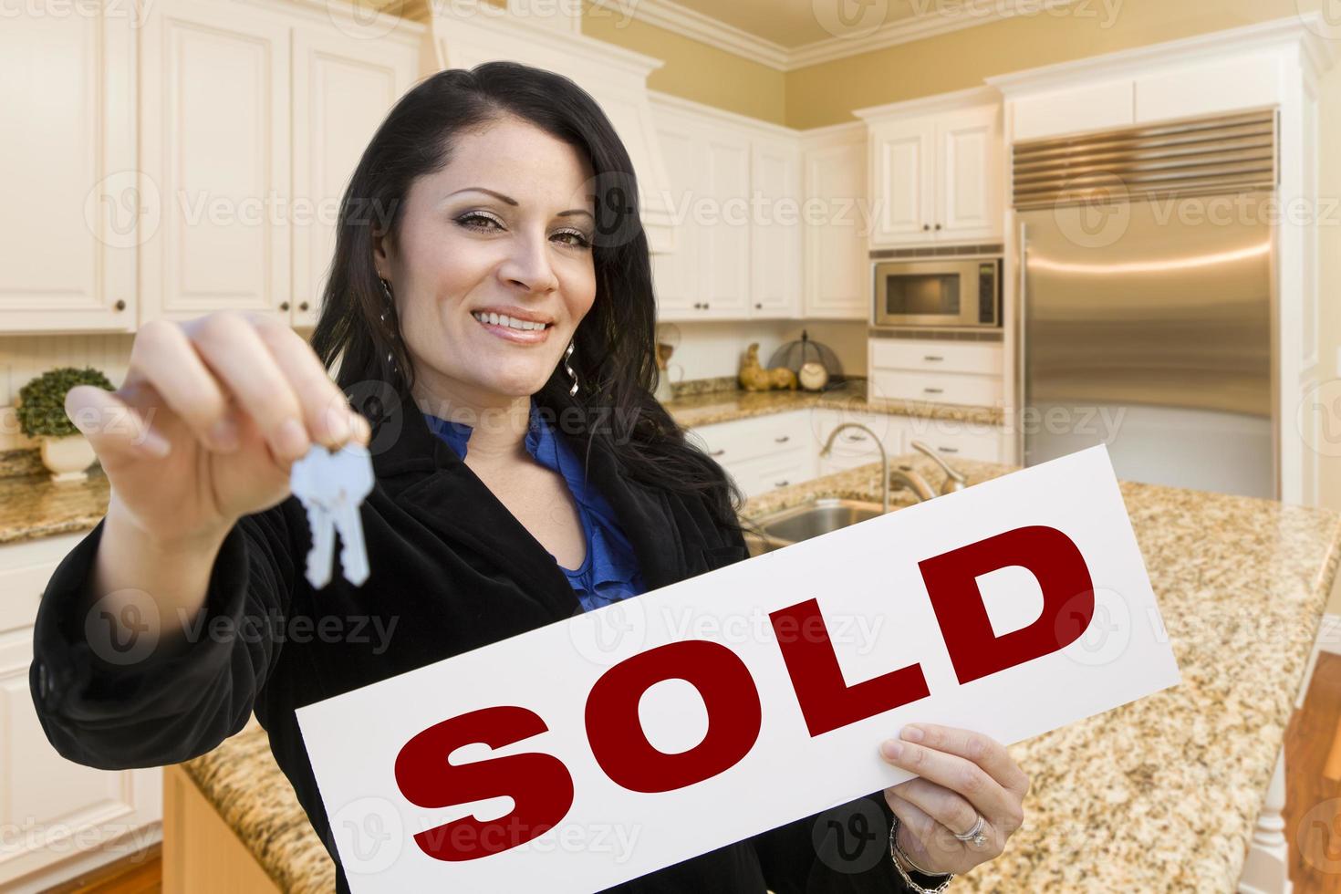 Hispanic Woman In Kitchen Holding House Keys and Sold Sign photo