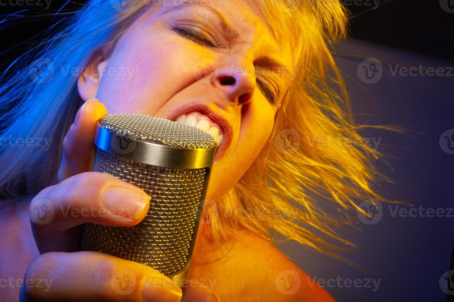 Female vocalist under gelled lighting sings with passion into condenser microphone. photo