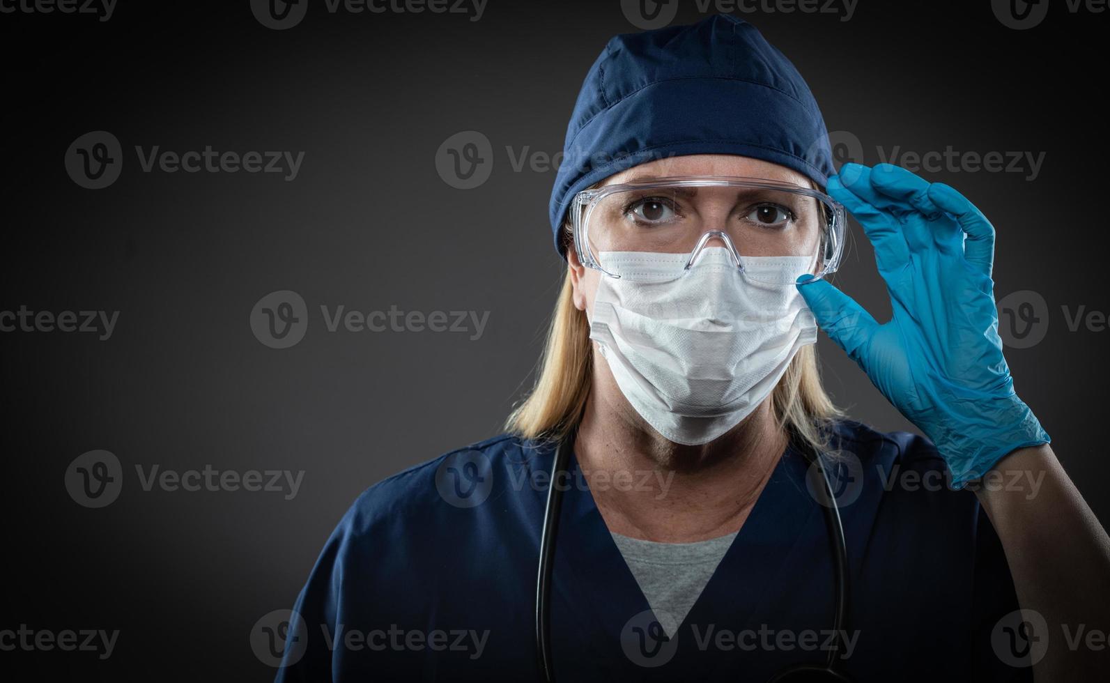 Female Medical Worker Wearing Protective Face Mask and Gear Against Dark Background photo