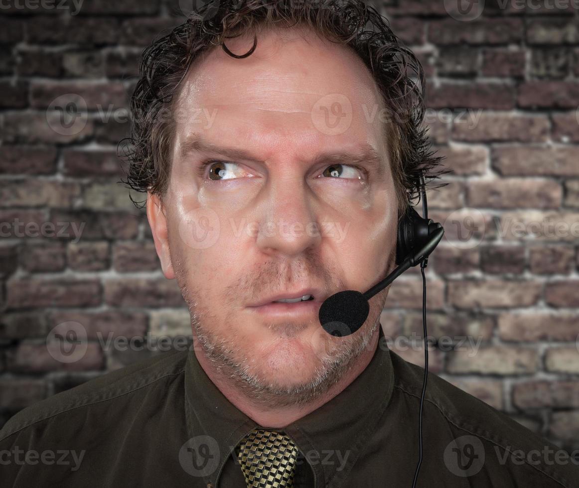 Unfriendly Confused Businessman with Frowning Face Wearing Phone Headset In Office with Brick Background photo