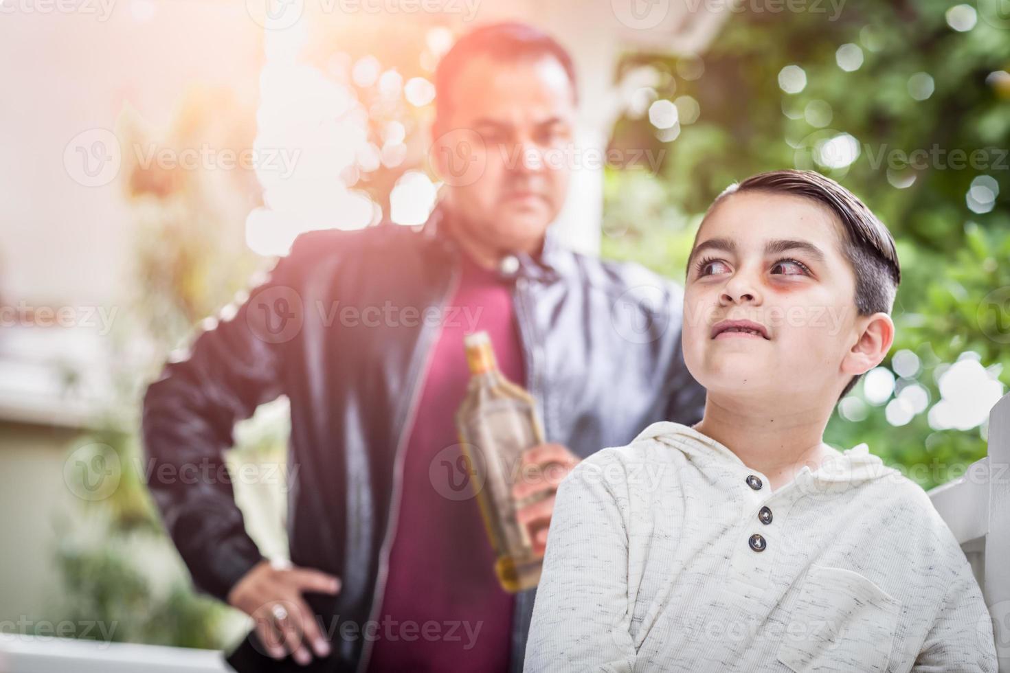 niño de raza mixta asustado y magullado frente a un hombre enojado que sostiene una botella de alcohol foto