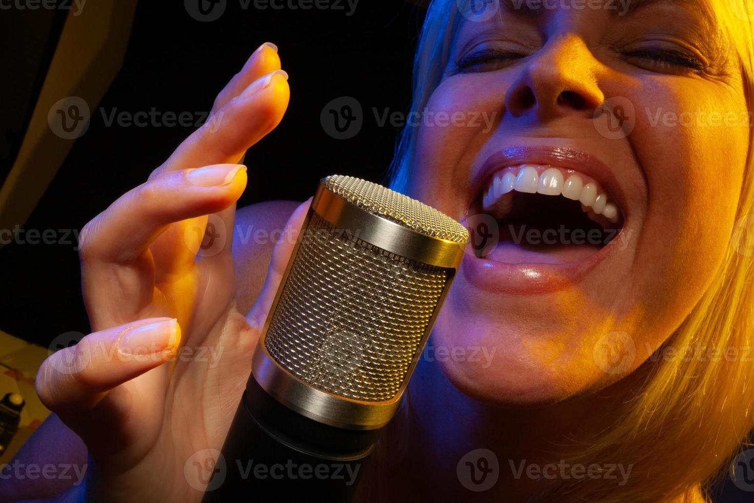 Female vocalist under gelled lighting sings with passion into condenser microphone. photo