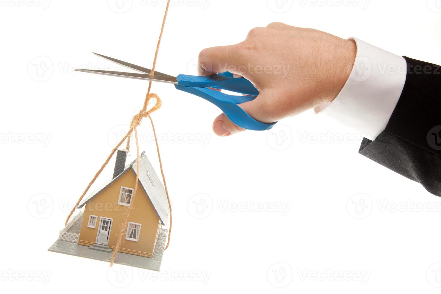 mano con tijeras cortando cuerda sosteniendo casa foto