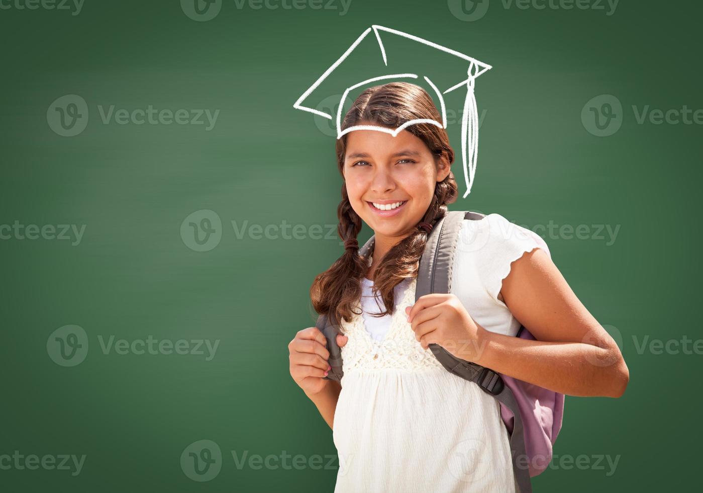 Young Hispanic Student Girl Wearing Backpack Front Of Blackboard with Fireman Helmet Drawn In Chalk Over Head photo