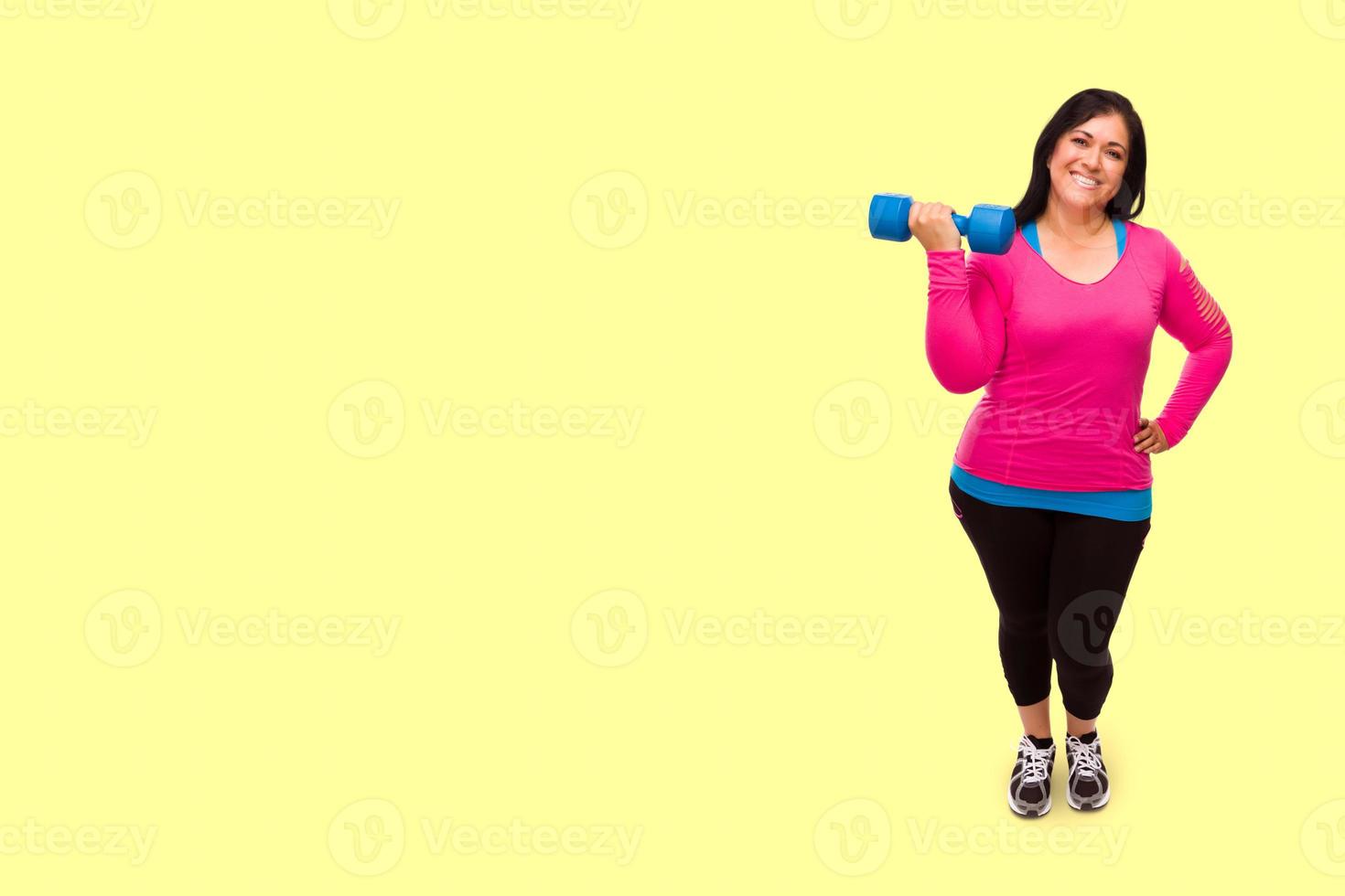mujer hispana de mediana edad con ropa de entrenamiento sosteniendo pesas contra un fondo amarillo brillante foto