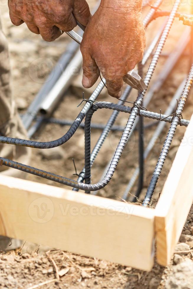 Trabajador que asegura la estructura de barras de refuerzo de acero con la herramienta de corte de alicates de alambre en el sitio de construcción foto