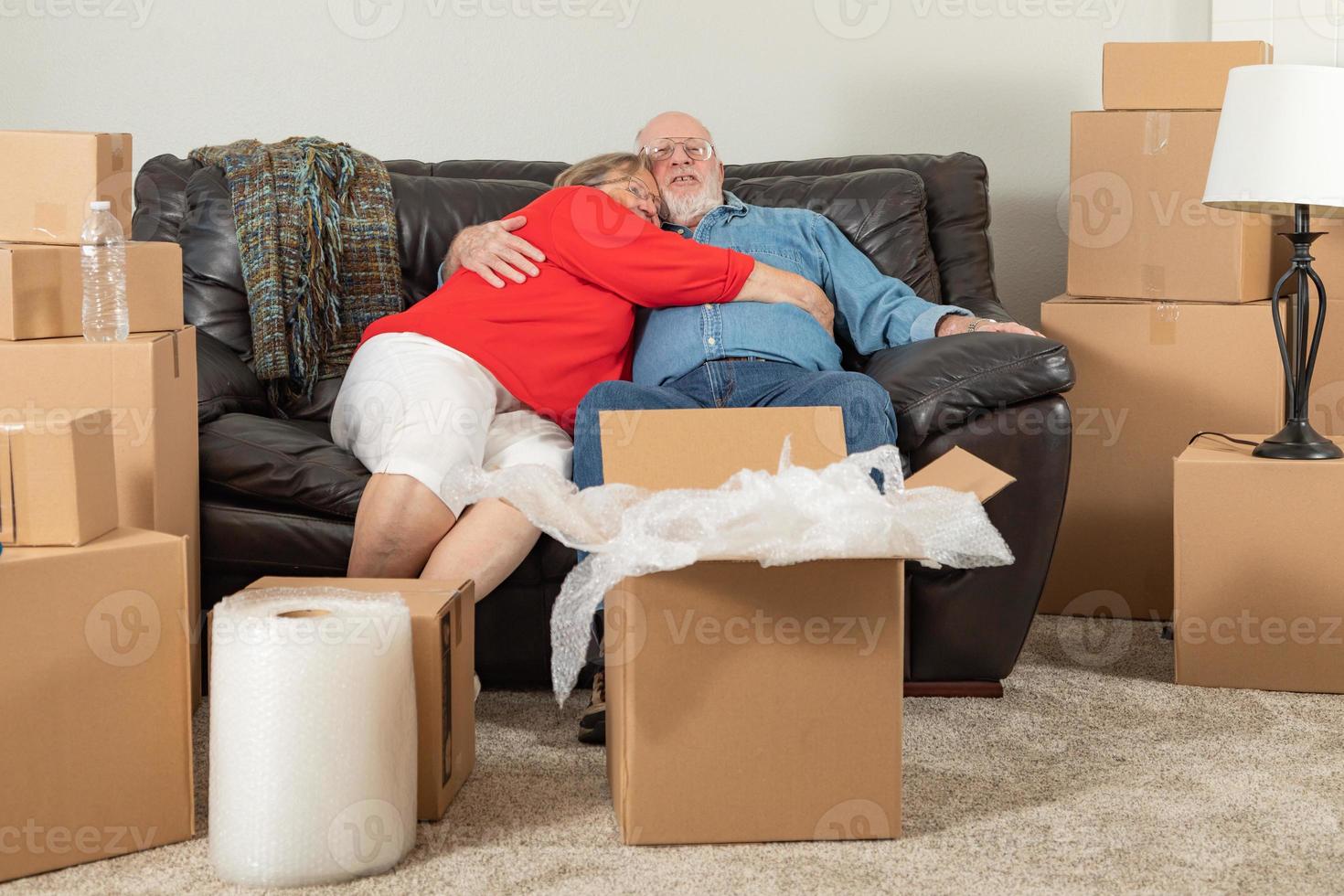 Affectionate Tired Senior Adult Couple Resting on Couch Surrounded By Moving Boxes photo