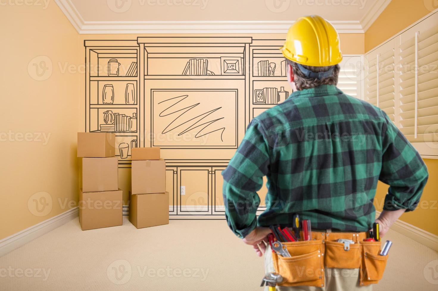Contractor Standing Indoors with Moving Boxes Looking At Line Drwaing of Entertainment Unit on Wall. photo