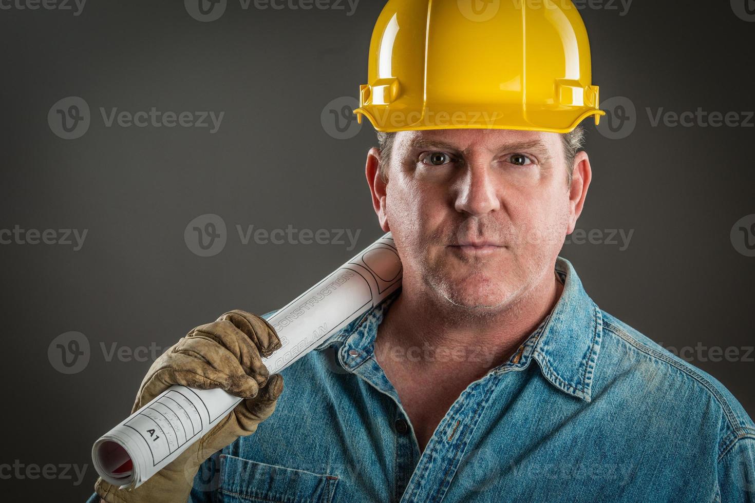 Serious Contractor in Hard Hat Holding Floor Plans With Dramatic Lighting. photo