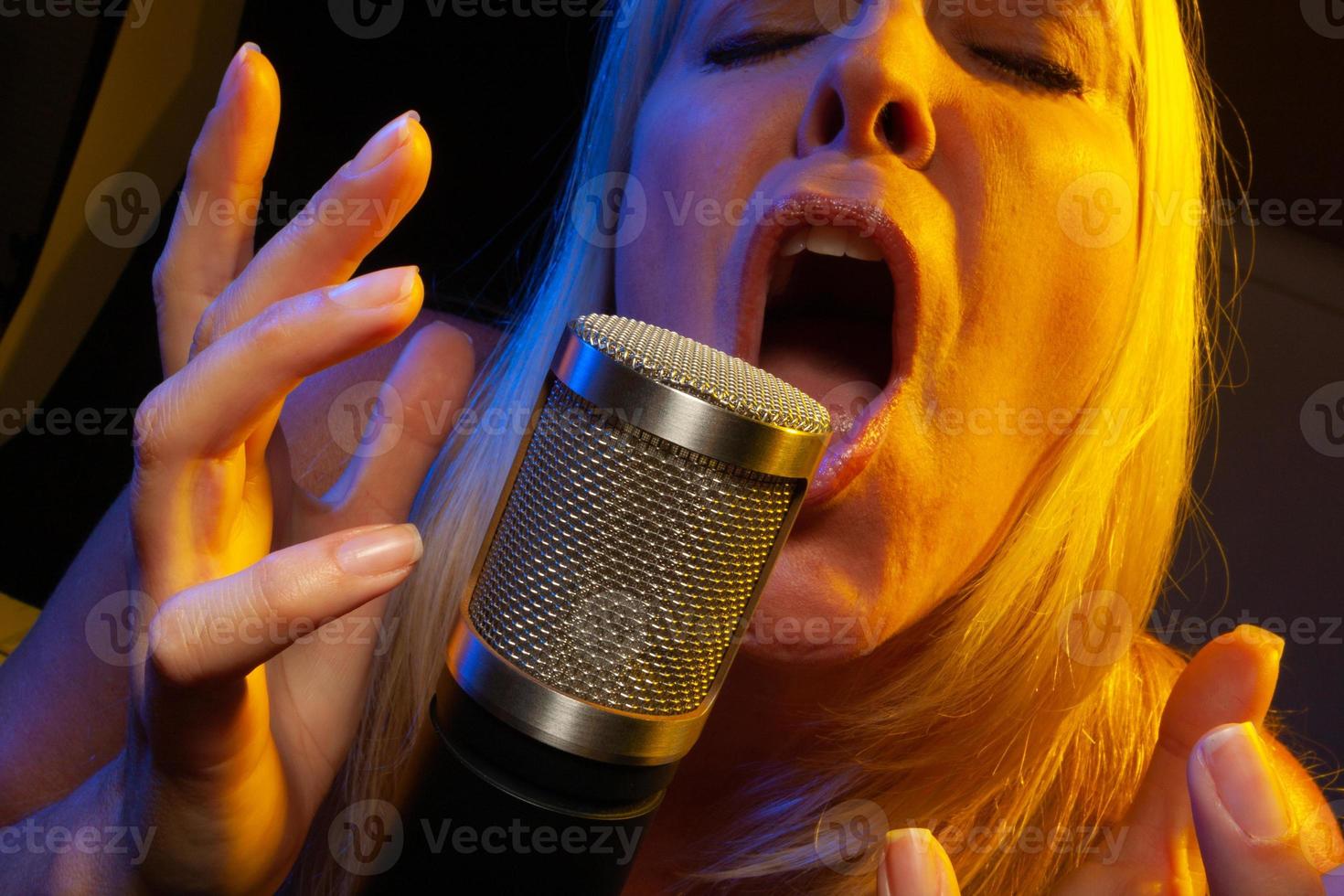 Female vocalist under gelled lighting sings with passion into condenser microphone. photo