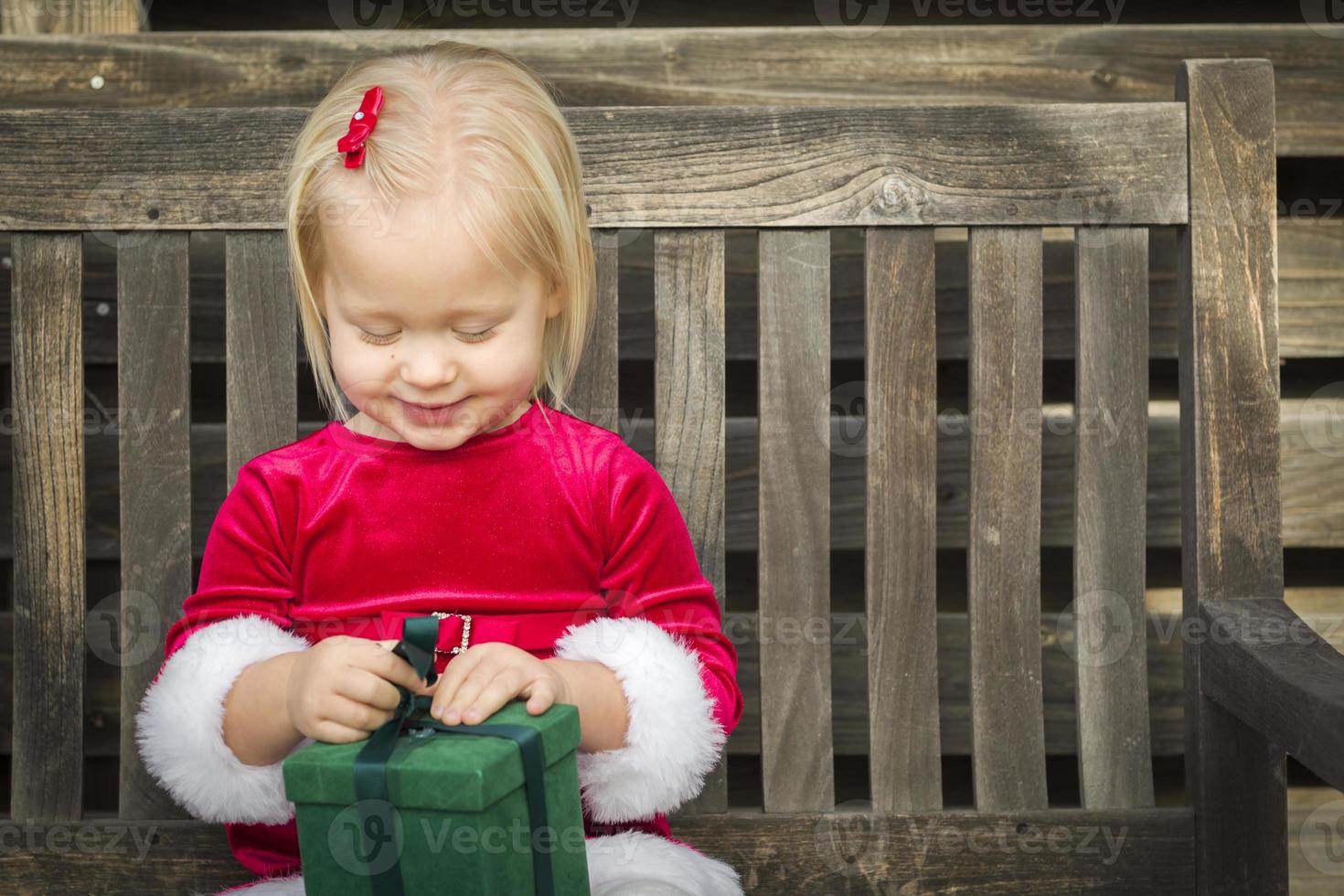 Adorable Little Girl Unwrapping Her Gift on a Bench photo