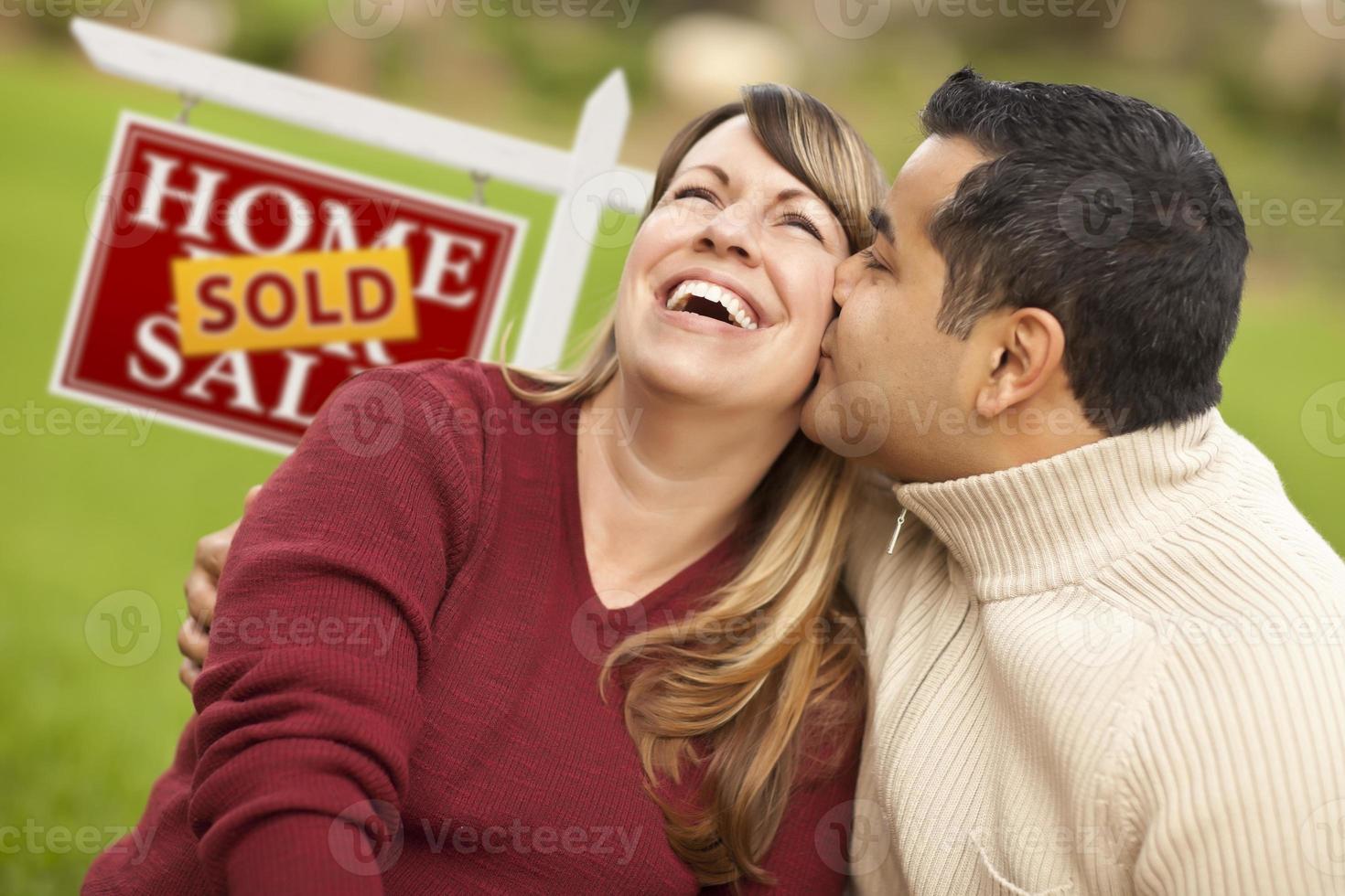 pareja de raza mixta frente al cartel de bienes raíces vendidos foto