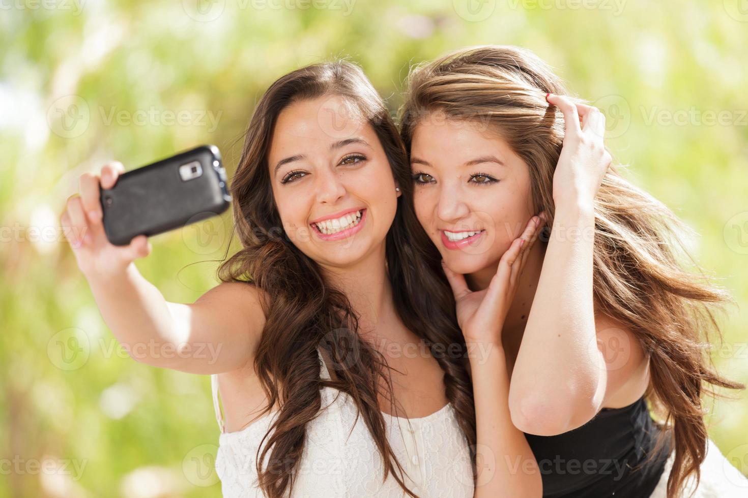 dos atractivas novias de raza mixta usando sus teléfonos celulares inteligentes para selfie al aire libre foto