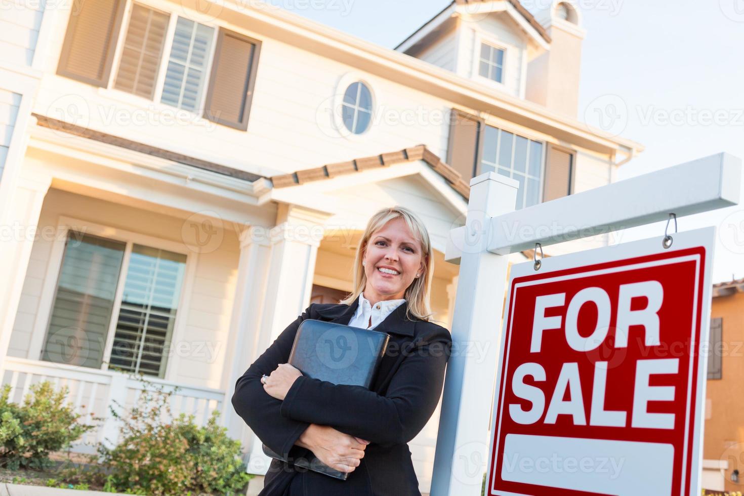 agente inmobiliaria femenina frente a un cartel de venta y una hermosa casa foto