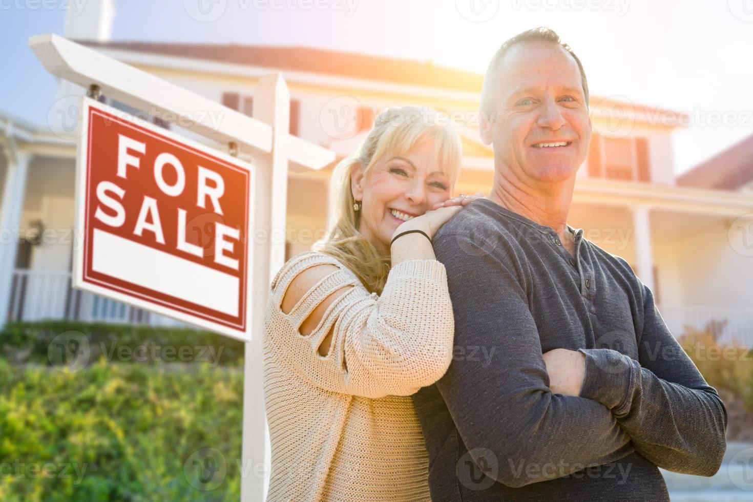 atractiva pareja de mediana edad en frente de la casa y en venta signo de bienes raíces foto