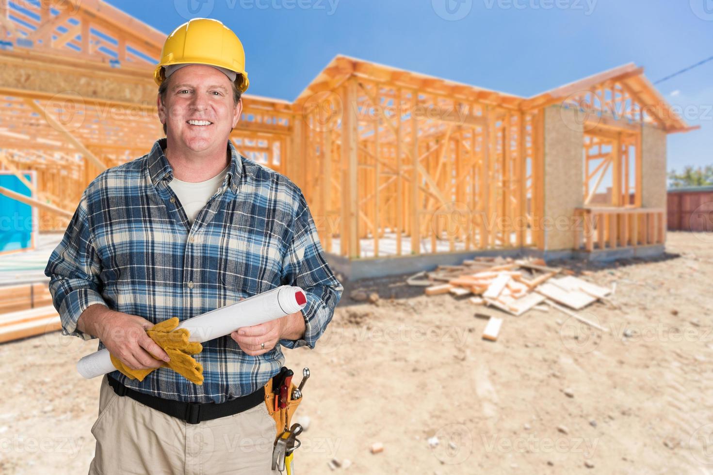 Male Contractor With House Plans Wearing Hard Hat In Front of New House Construction Framing photo