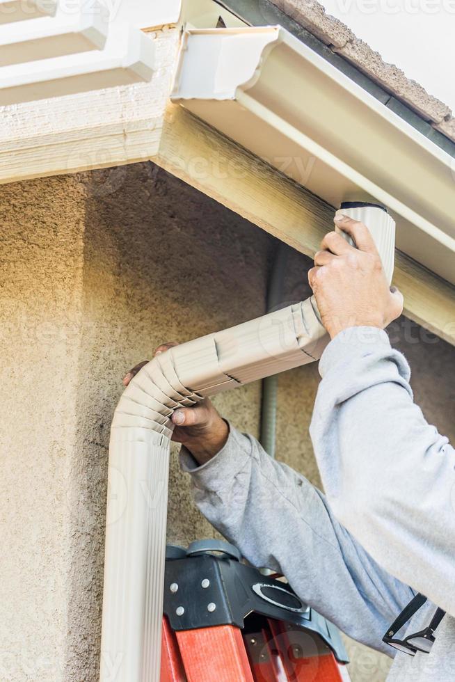 trabajador colocando un canalón de lluvia de aluminio y un canalón hacia abajo a la fascia de la casa foto