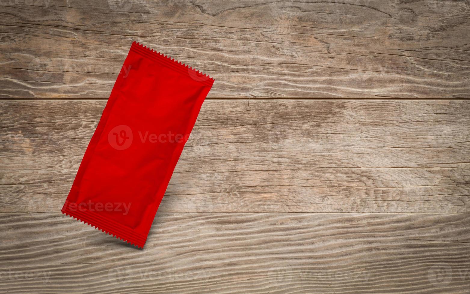 Blank Red Condiment Packet Floating on Aged Wood Background photo