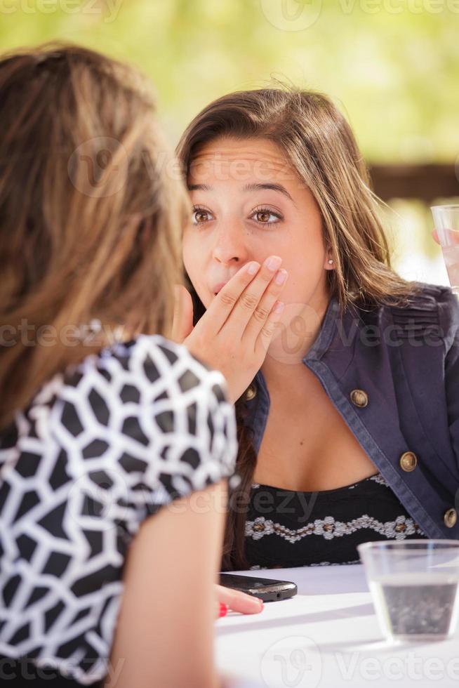 Expressive Young Adult Woman Having Drinks and Talking with Her Friend Outdoors photo