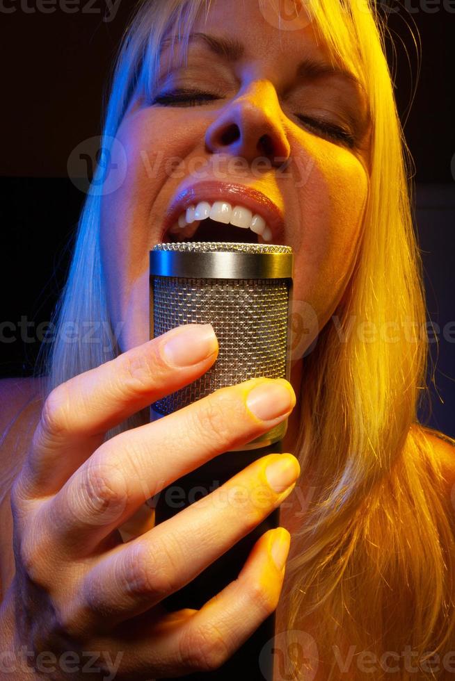 Female vocalist under gelled lighting sings with passion into condenser microphone. photo