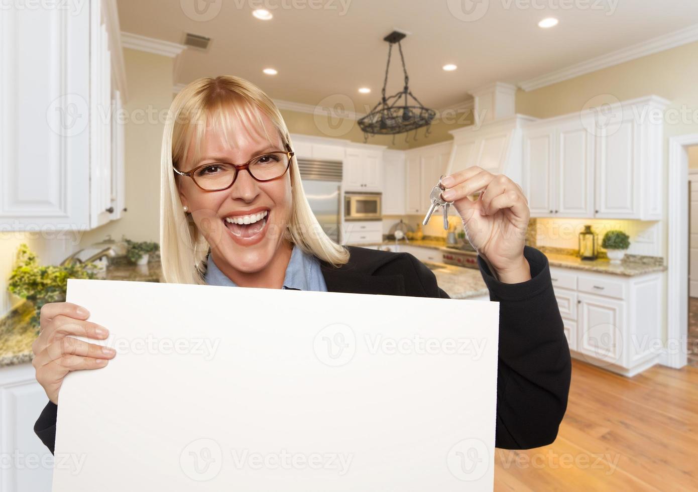 mujer joven sosteniendo un cartel en blanco y llaves dentro de la cocina foto