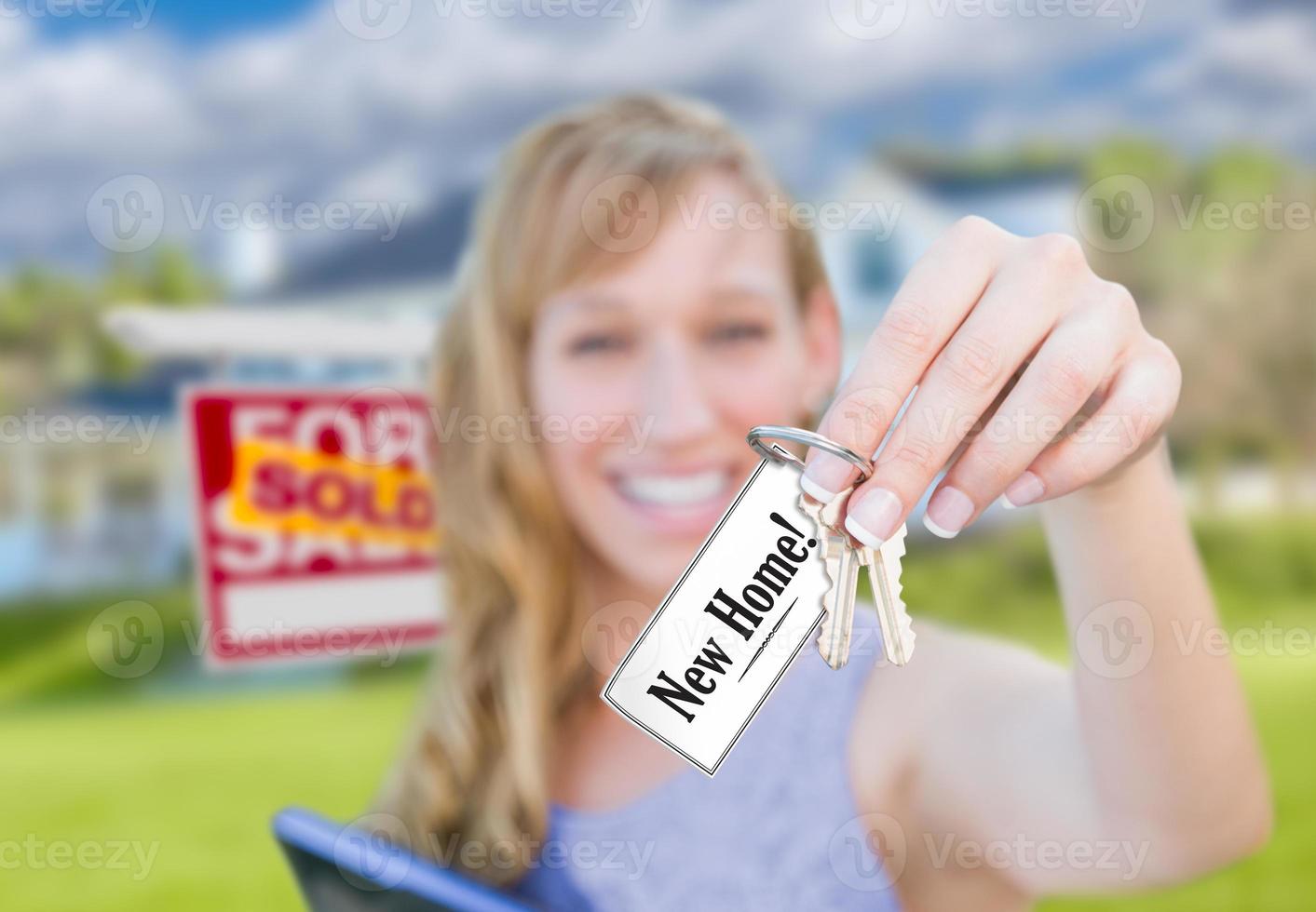 Woman Holding New House Keys with New Home Card In Front of Sold Real Estate Sign and Home. photo