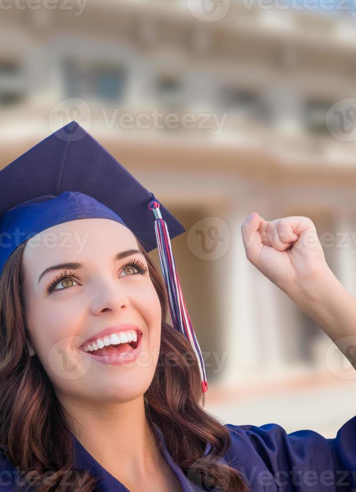 feliz graduada mujer de raza mixta en toga y birrete celebrando en el campus. foto