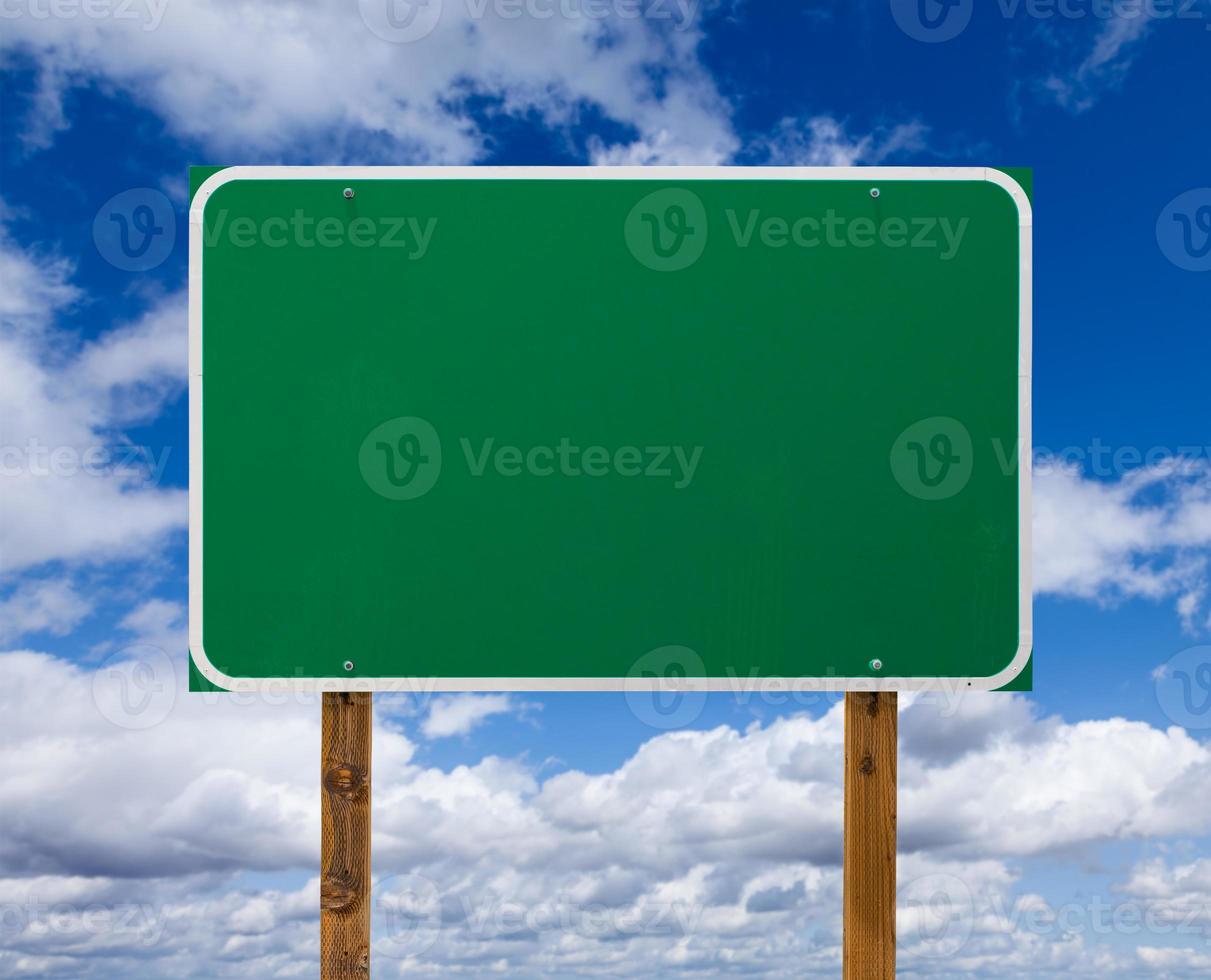 Blank Green Road Sign with Wooden Posts Over Blue Sky and Clouds photo