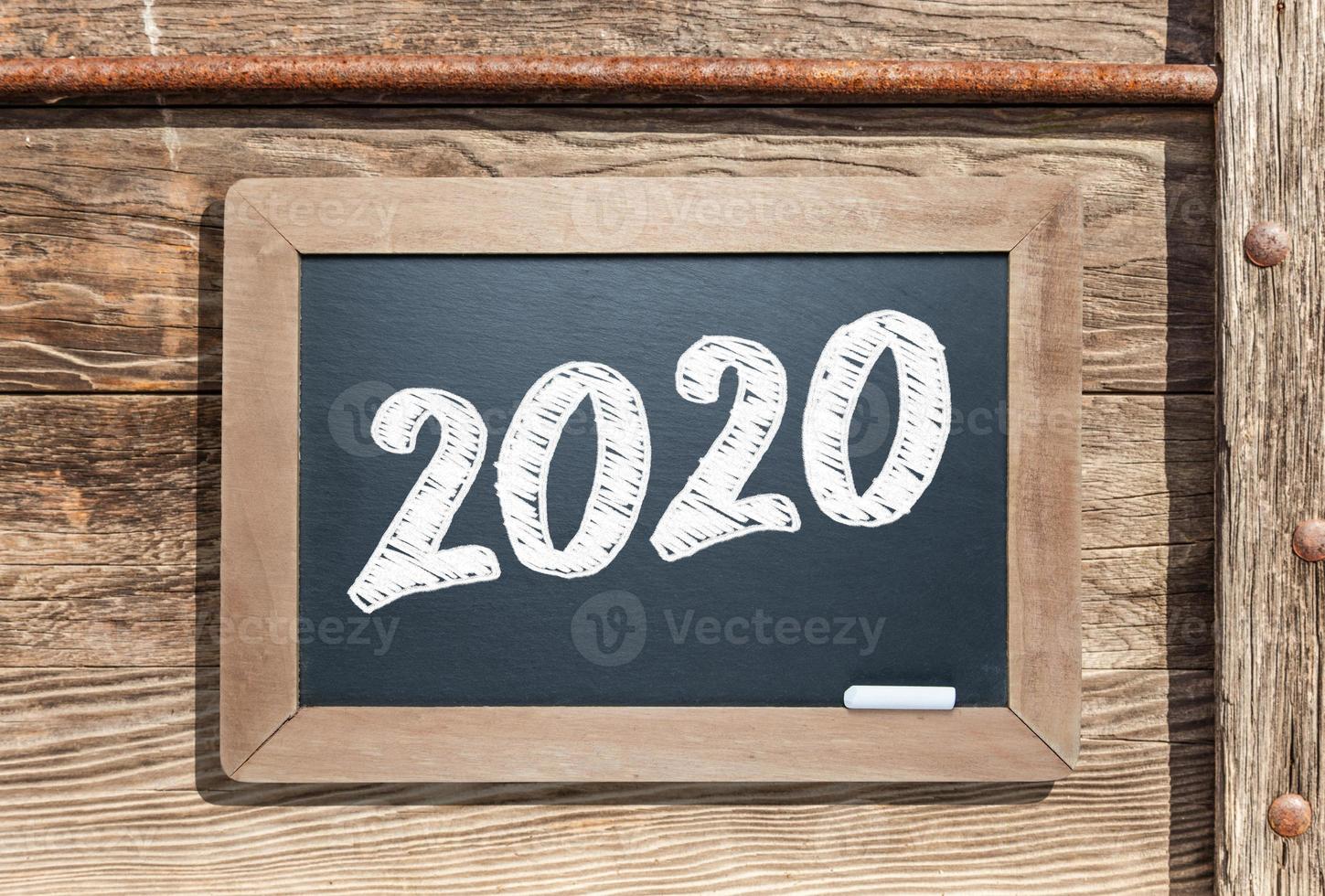 2020 Written on Slate Chalk Board Against Aged Wood and Pipe Background photo