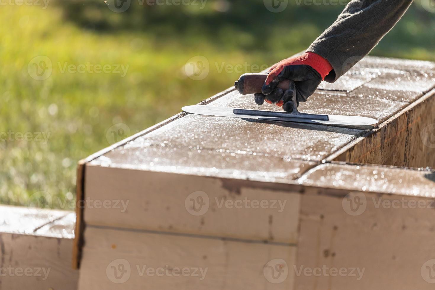 trabajador de la construcción usando paleta sobre cemento húmedo formando afrontamiento alrededor de la nueva piscina foto