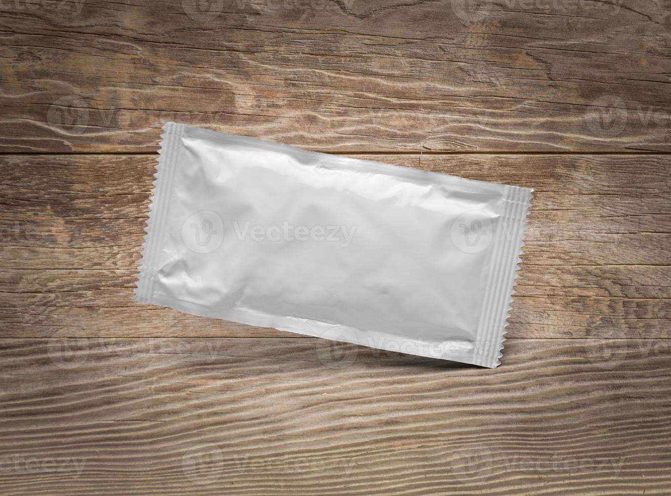 Blank White Condiment Packet Floating on Aged Wood Background photo