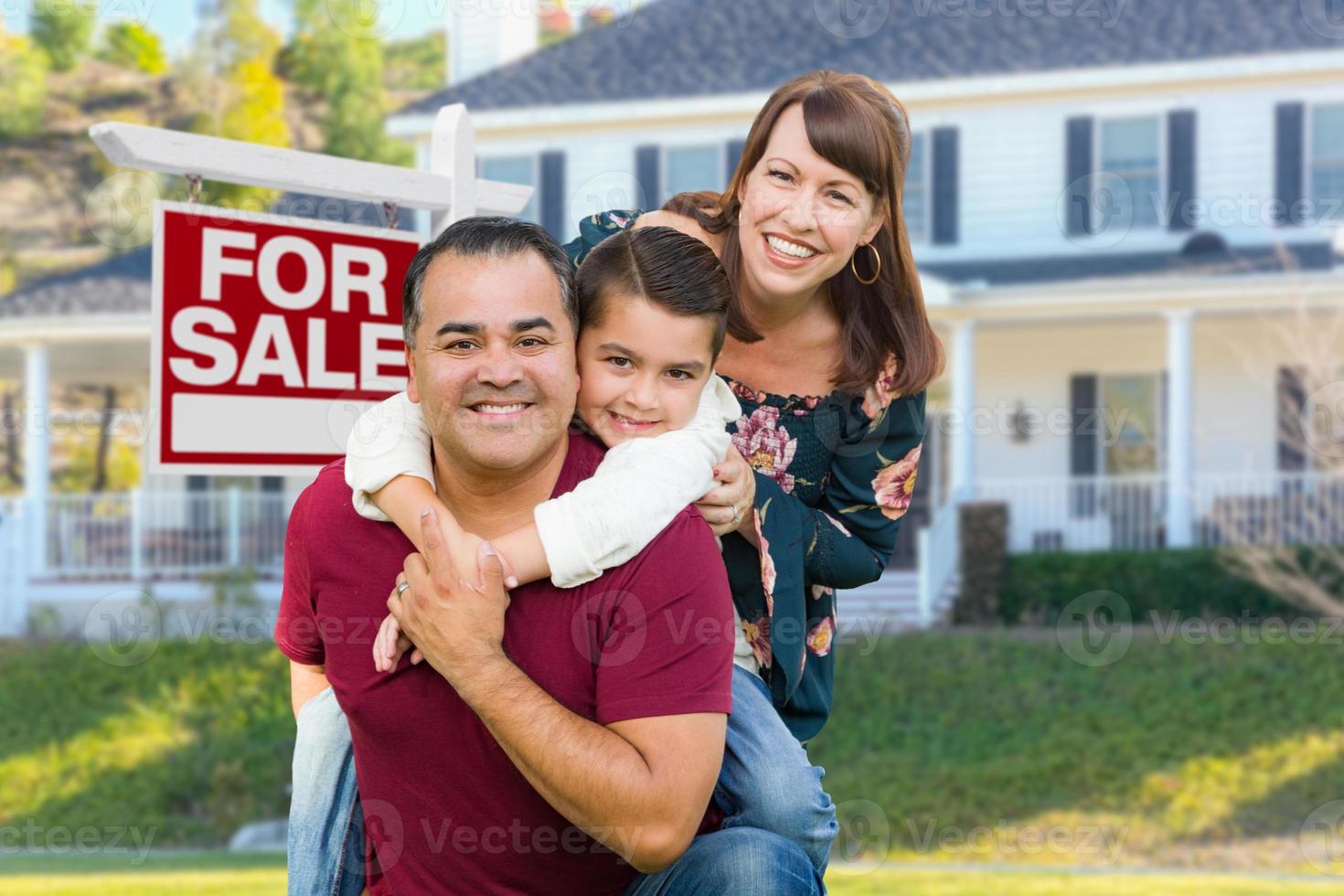 feliz familia de raza mixta frente a la casa y en venta signo de bienes raíces foto
