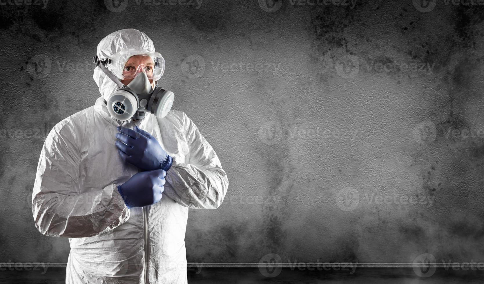 Man Wearing Hazmat Suit, Protective Gas Mask and Goggles Against Dark Wall photo