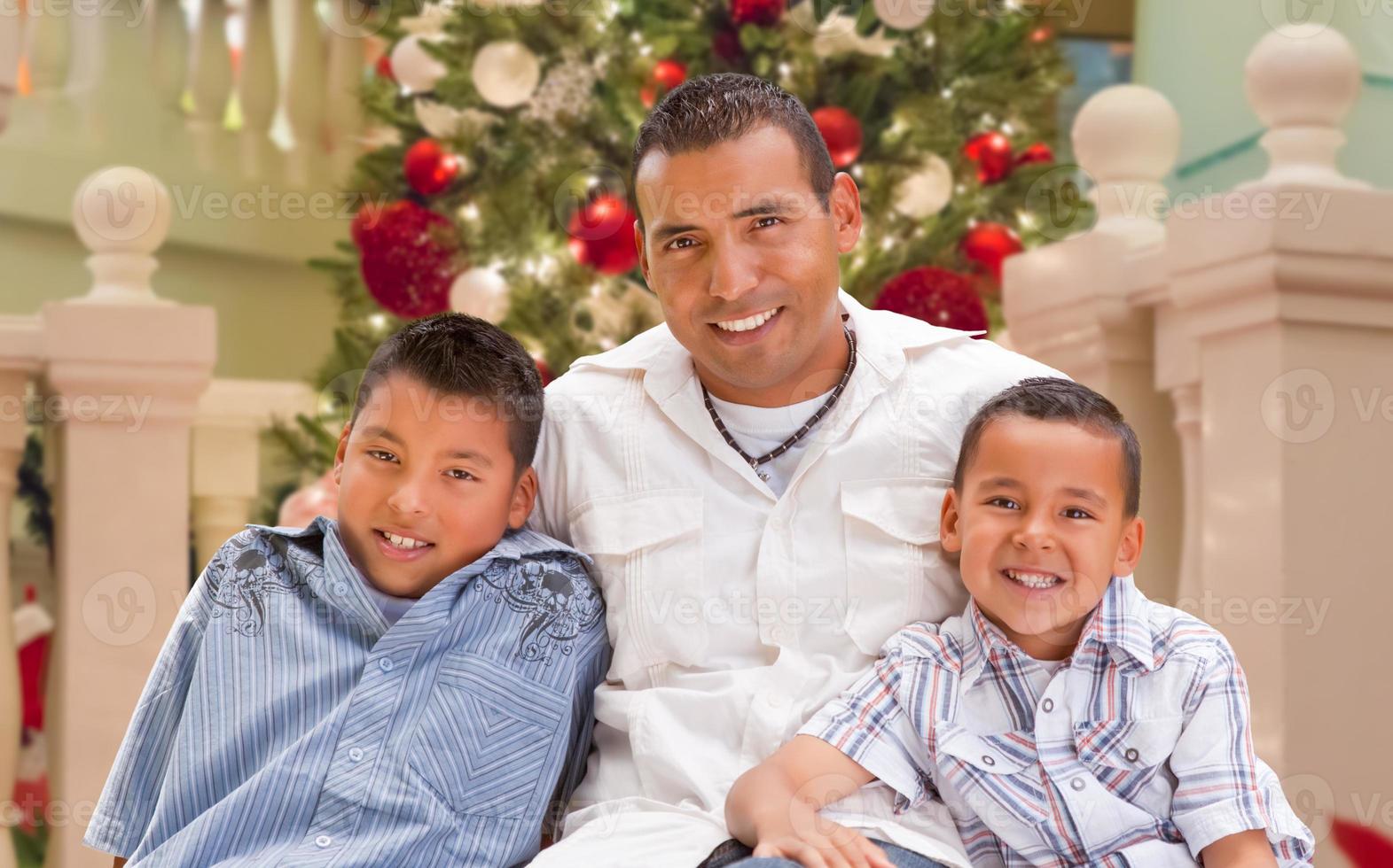 Hispanic Young Father and Sons In Front of Decorated Christmas Tree. photo