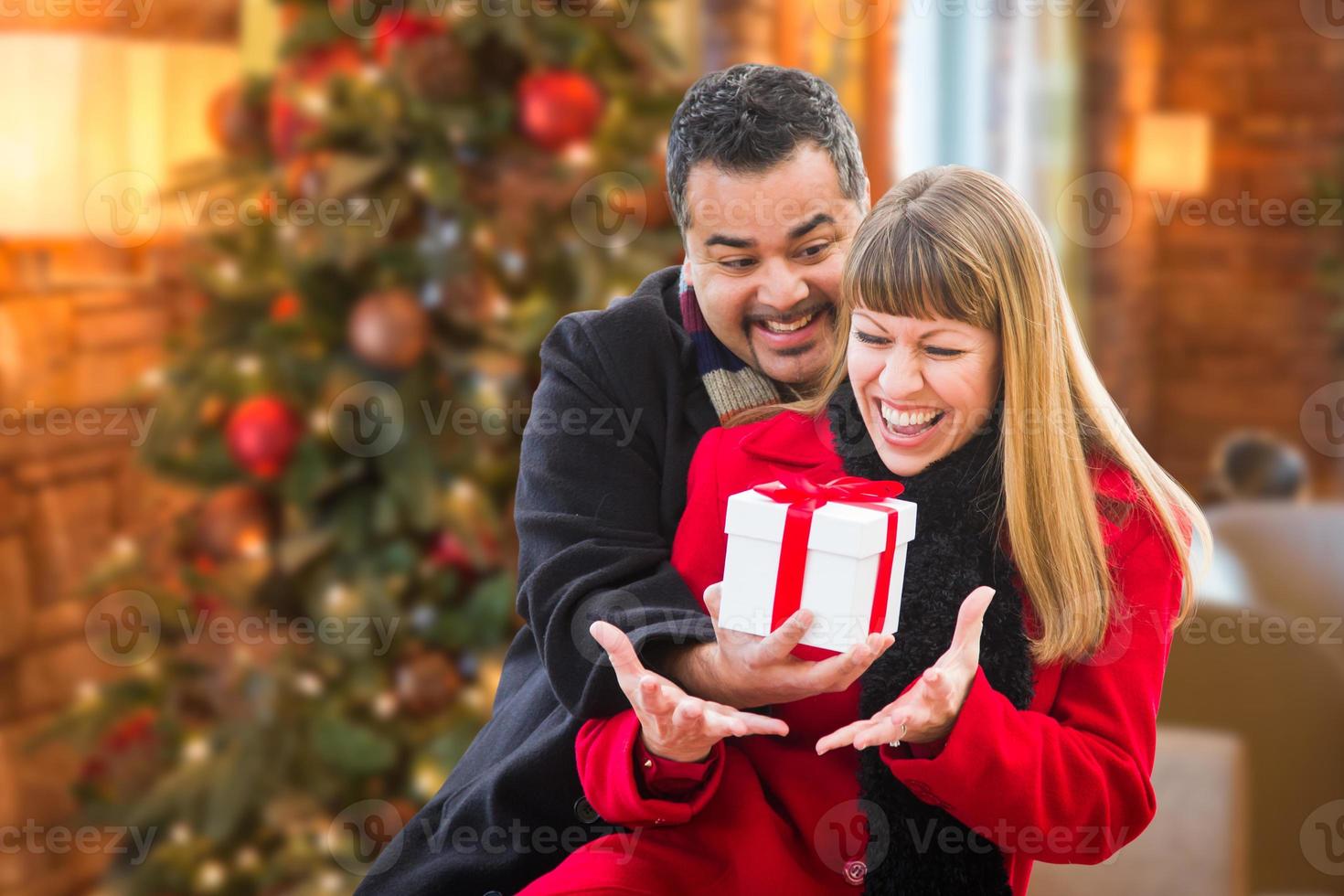 Mixed Race Couple Sharing Christmas In Front of Decorated Tree. photo