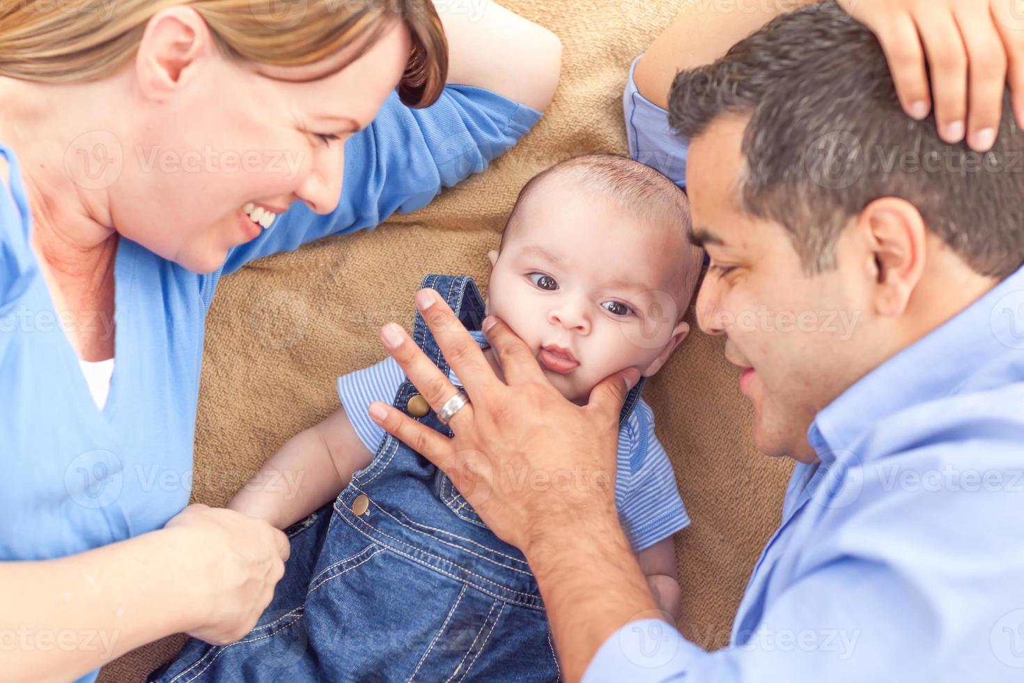 Young Mixed Race Couple Laying With Their Infant On A Blanket photo