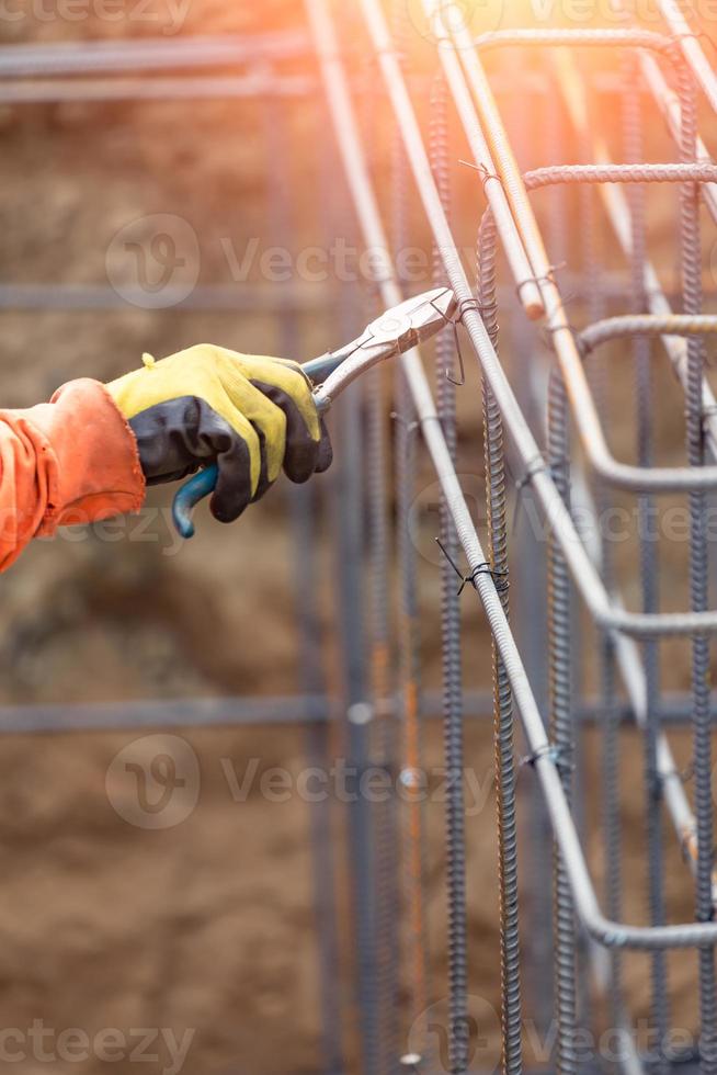 Worker Securing Steel Rebar Framing With Wire Plier Cutter Tool At Construction Site photo