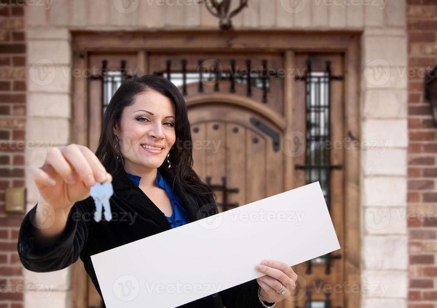 mujer hispana sosteniendo un cartel en blanco y llaves frente a la casa foto