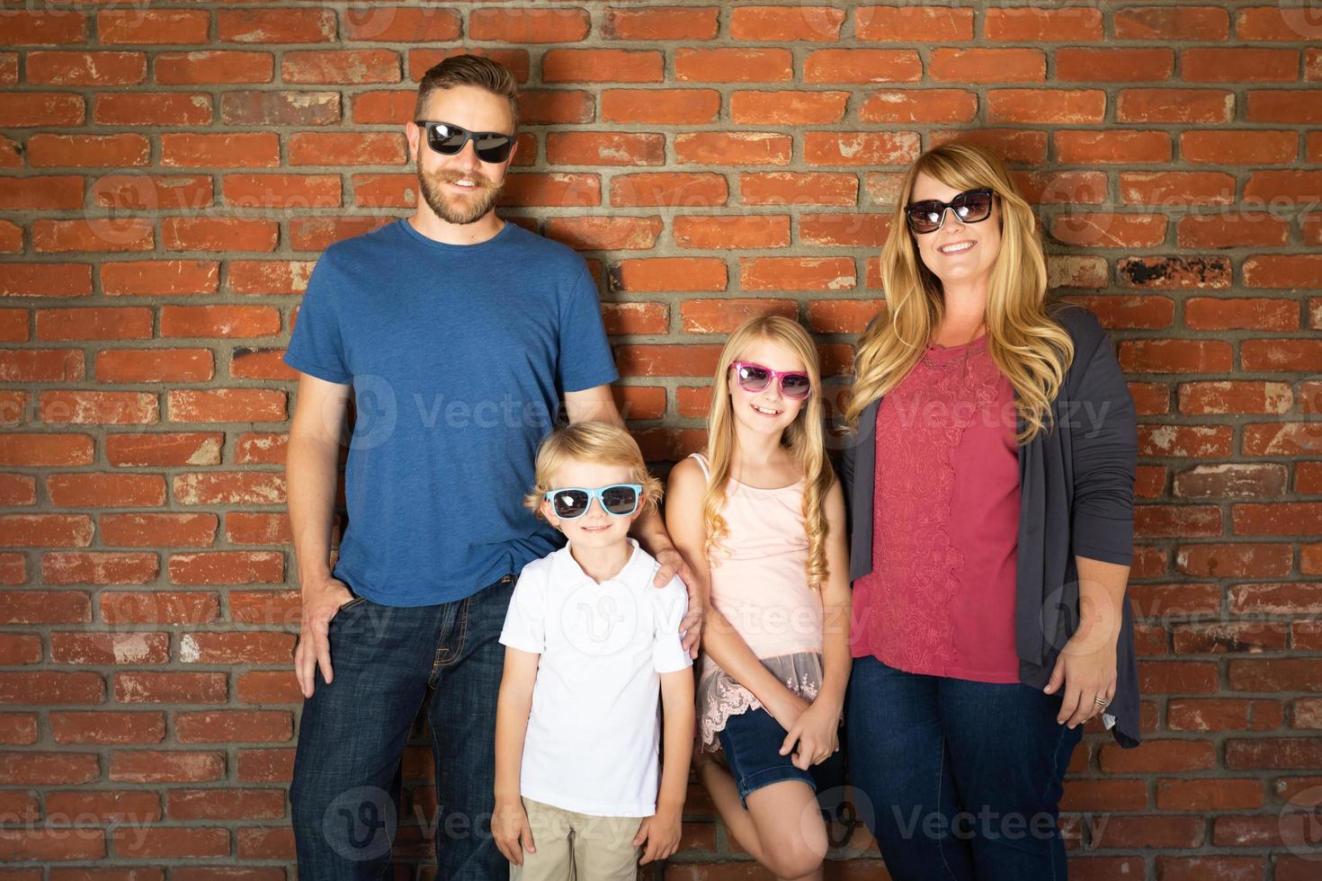 Young Caucasian Family Wearing Sunglasses Against Brick Wall photo