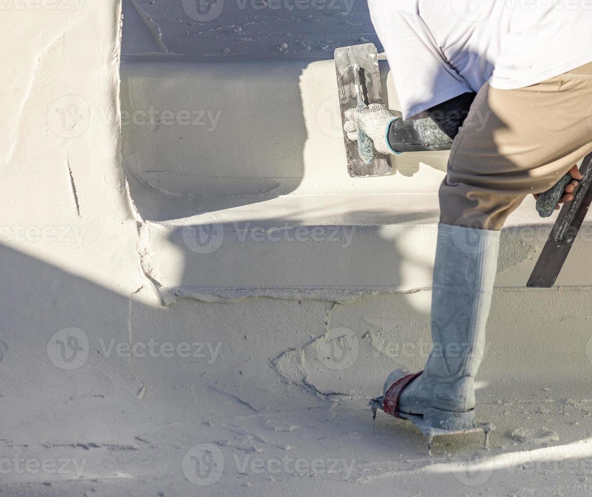 Worker Wearing Spiked Shoes Smoothing Wet Pool Plaster With Trowel photo