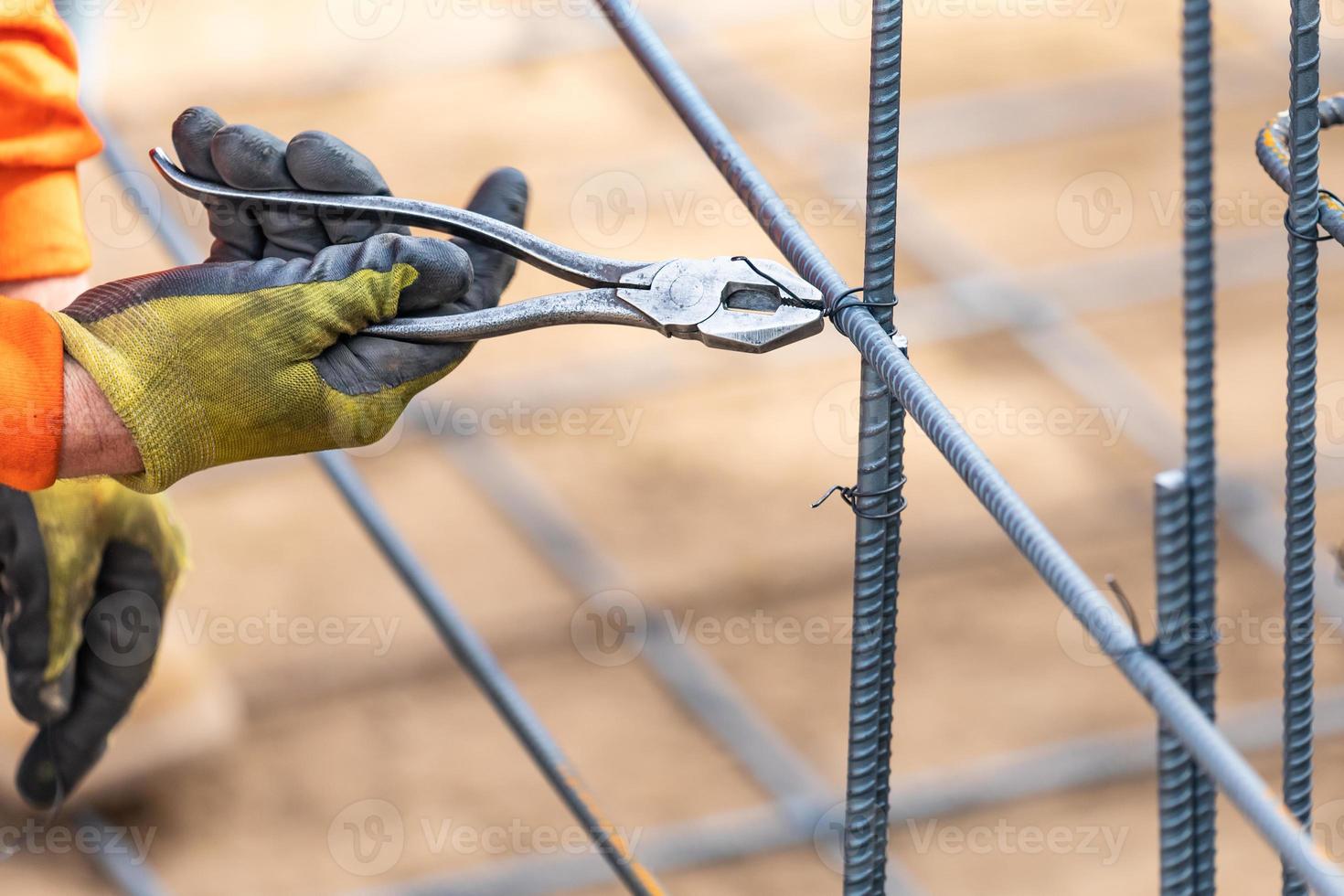 Trabajador que asegura la estructura de barras de refuerzo de acero con la herramienta de corte de alicates de alambre en el sitio de construcción foto