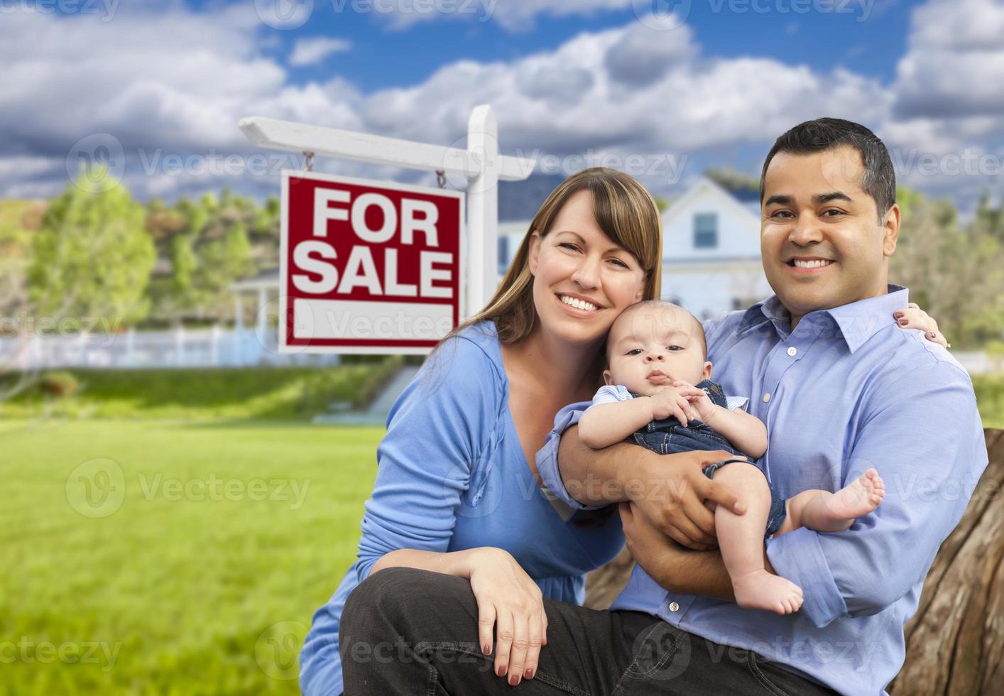 familia joven frente a la casa y el cartel de venta foto