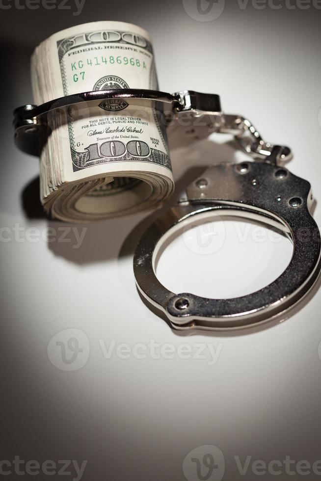 Handcuffs Locked on Roll of One Hundred Dollar Bills Under Spotlight photo