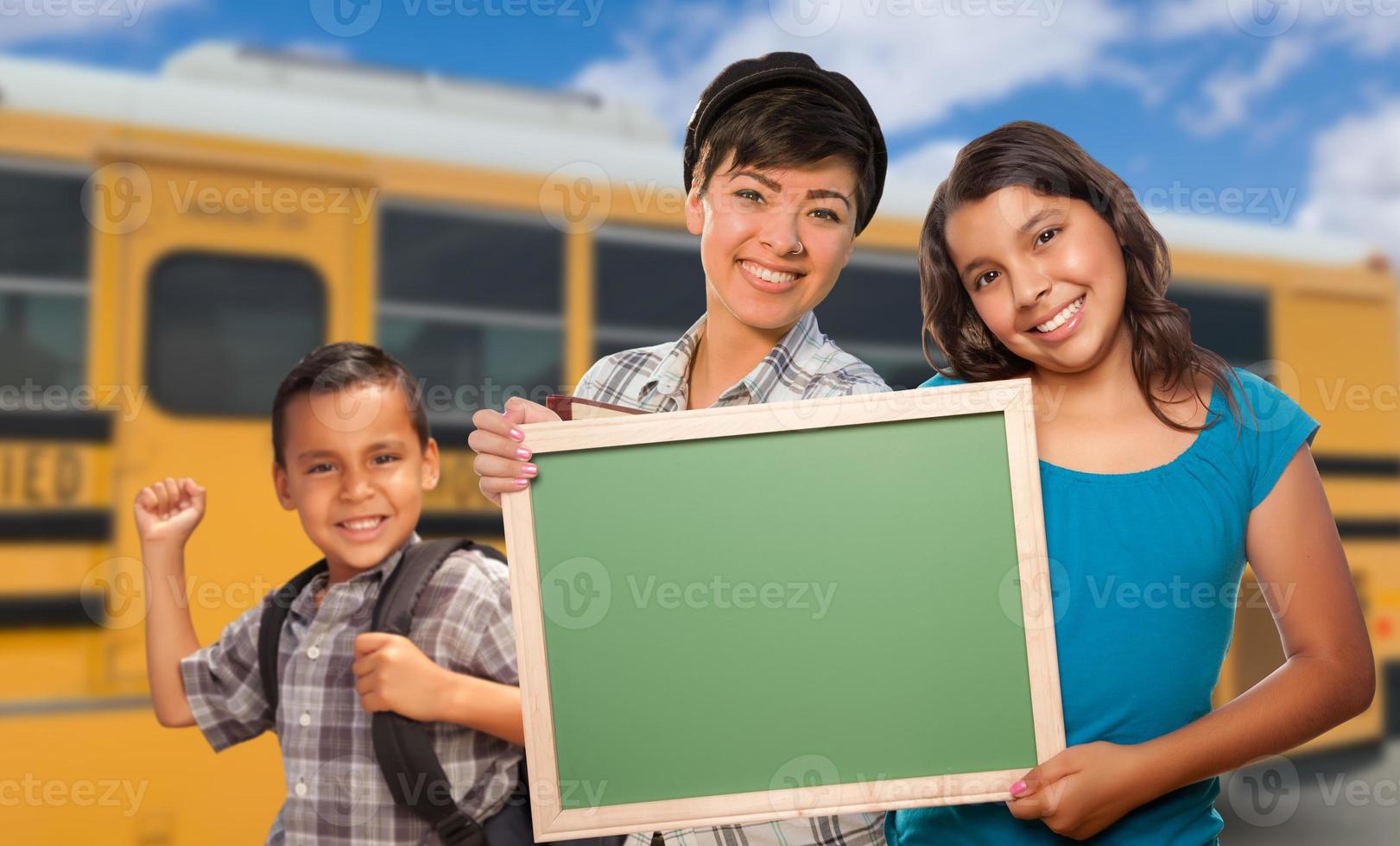 Young Mixed Race Students with Blank Chalkboard Near School Bus photo