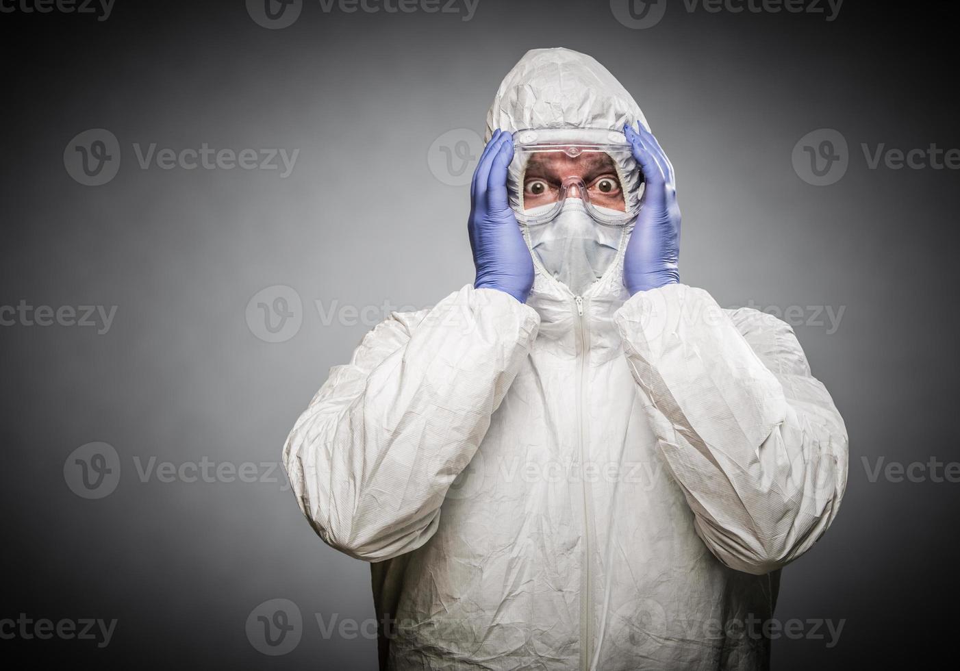 Man Holding Head With Hands Wearing HAZMAT Protective Clothing Against A Gray Background. photo