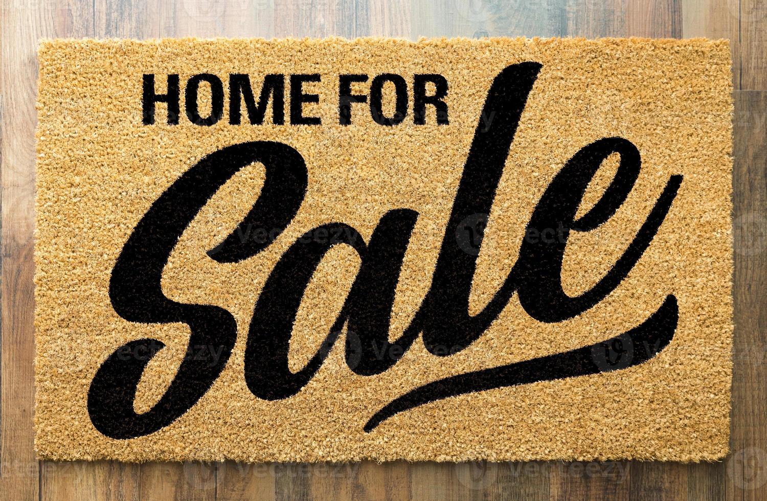 Home For Sale Welcome Mat On A Wood Floor Background photo