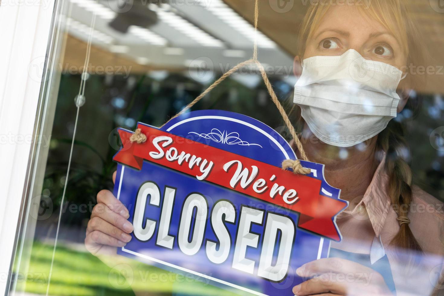 Female Store Owner Wearing Medical Face Mask Turning Sign to Closed in Window photo